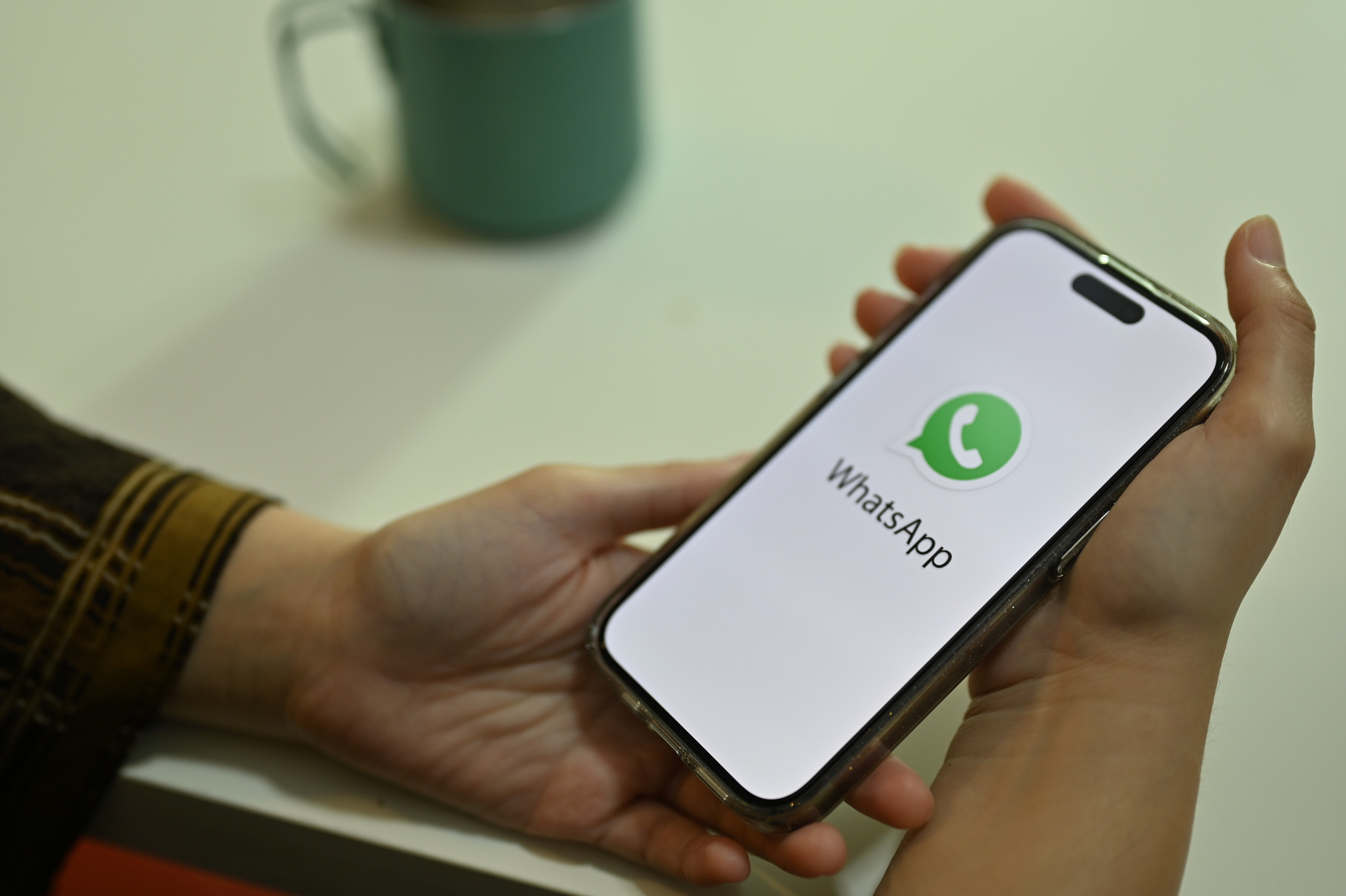 Female hands holding a smartphone white WhatsApp logo on screen.